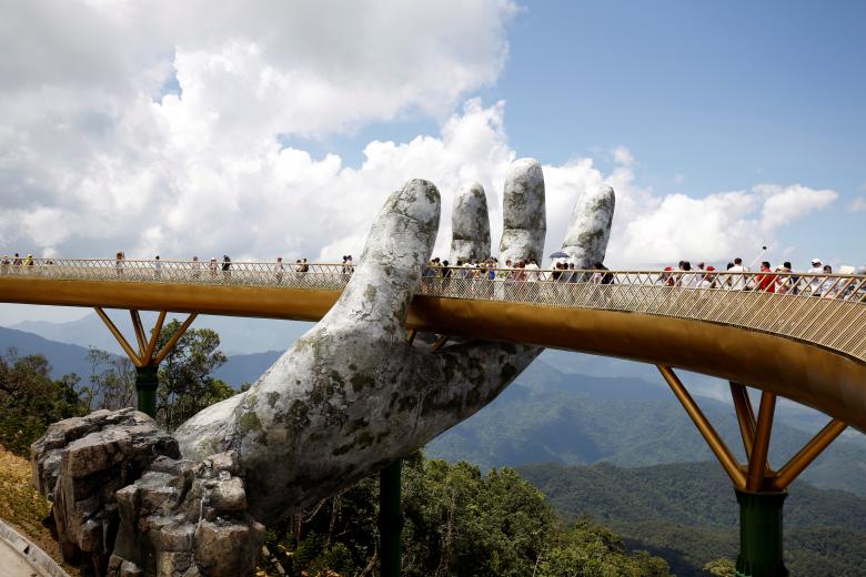 Tourists walk past giant hand structure on Gold Bridge on Ba Na hill near Danang City
