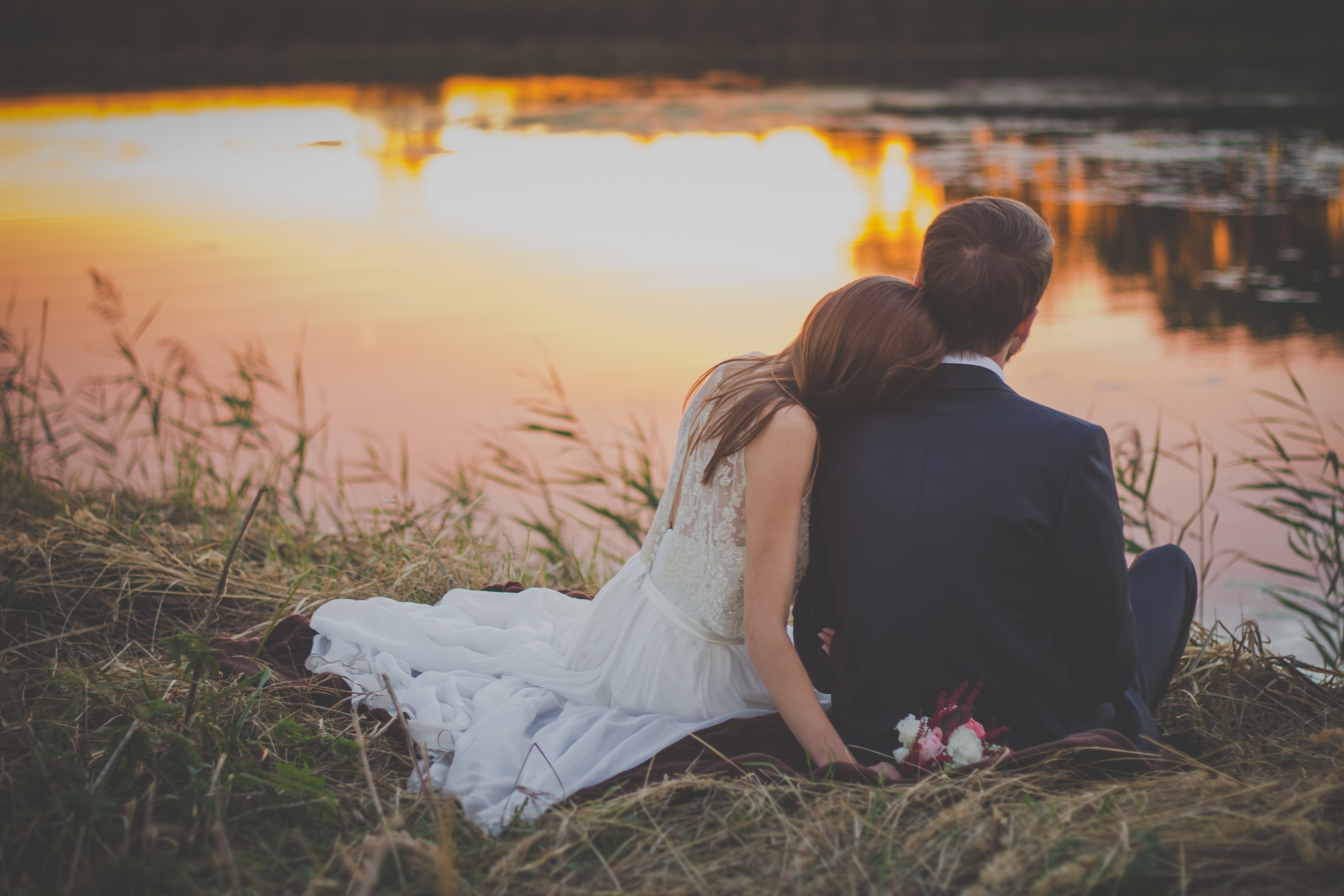 wedding-couple-sitting-on-green-grass-in-front-of-body-of-70737